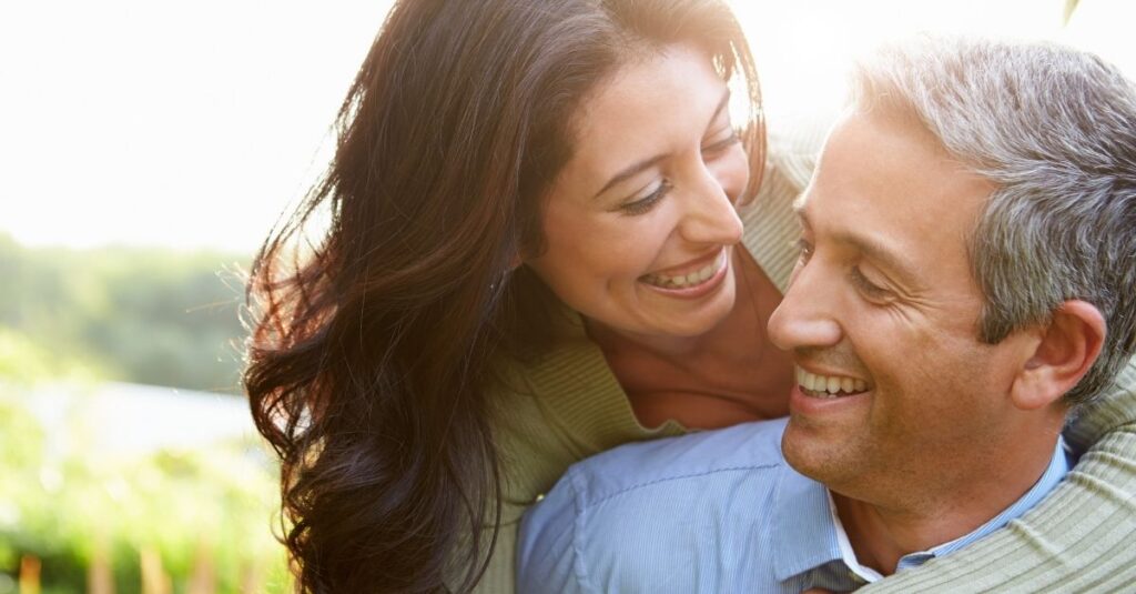 A happy couple smiles and laughs together outdoors.