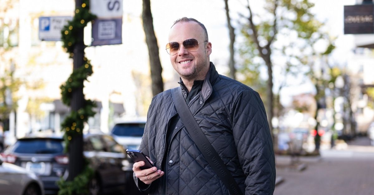 Dr. Mike, wearing a black jacket in an urban setting, looks at the camera, smiling.