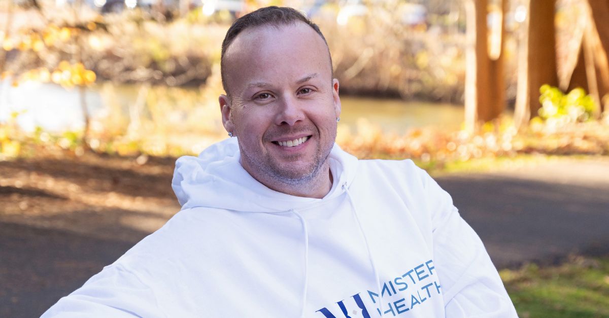 Dr. Mike sitting outside on a park bench wearing a Mister Health hoodie with a warm smile on his face.