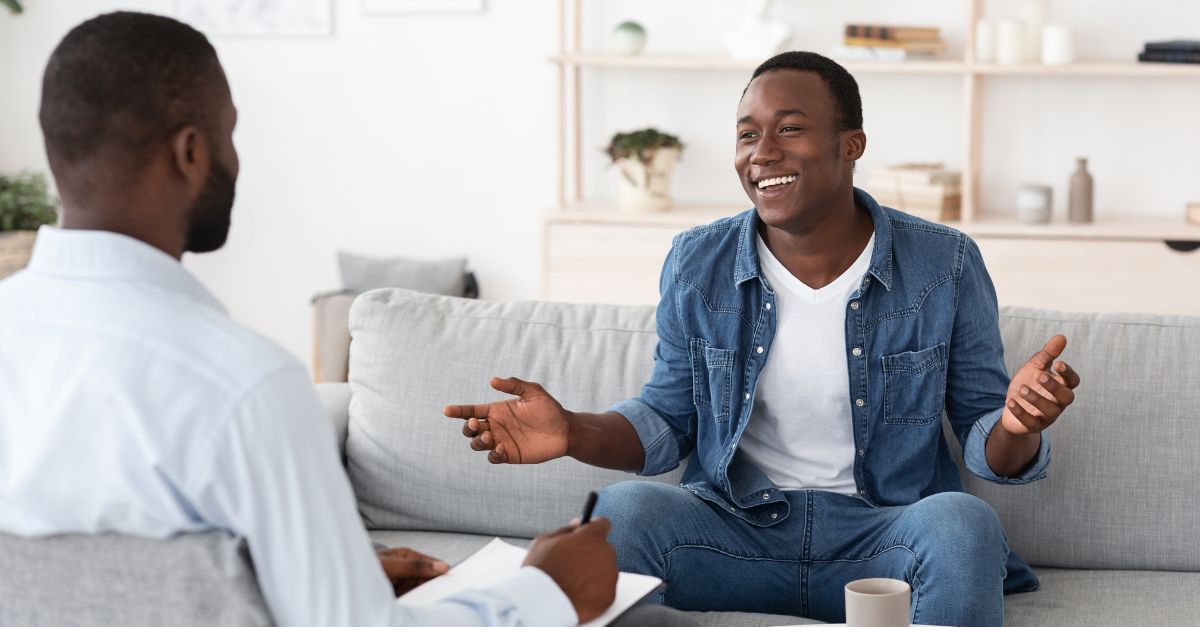 Smiling man sitting on a couch, talking openly with a therapist during a counseling session, representing trust, communication, and emotional well-being.