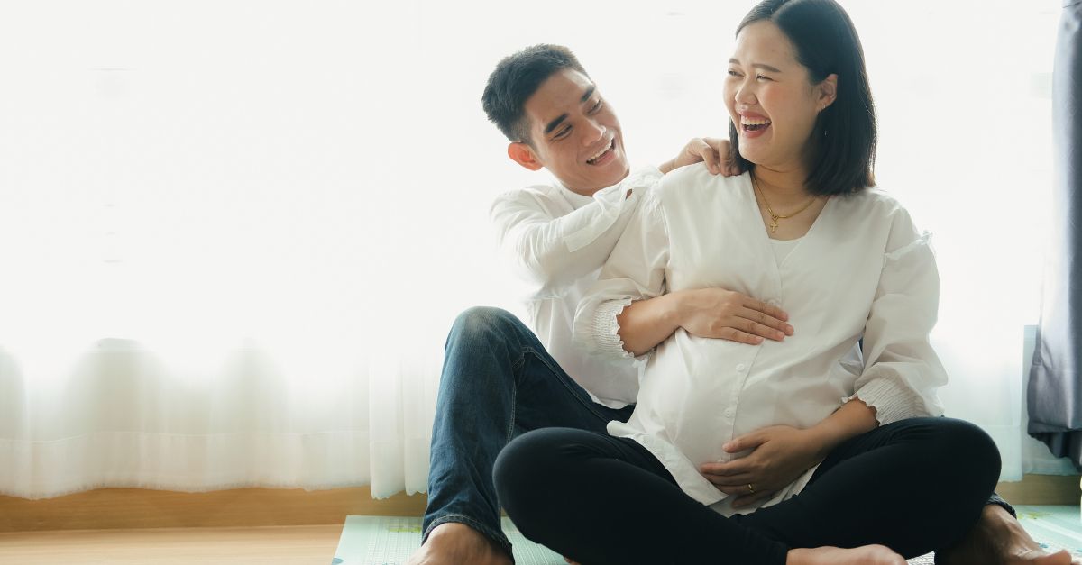 Expecting couple sharing a laugh together as the woman holds her pregnant belly.