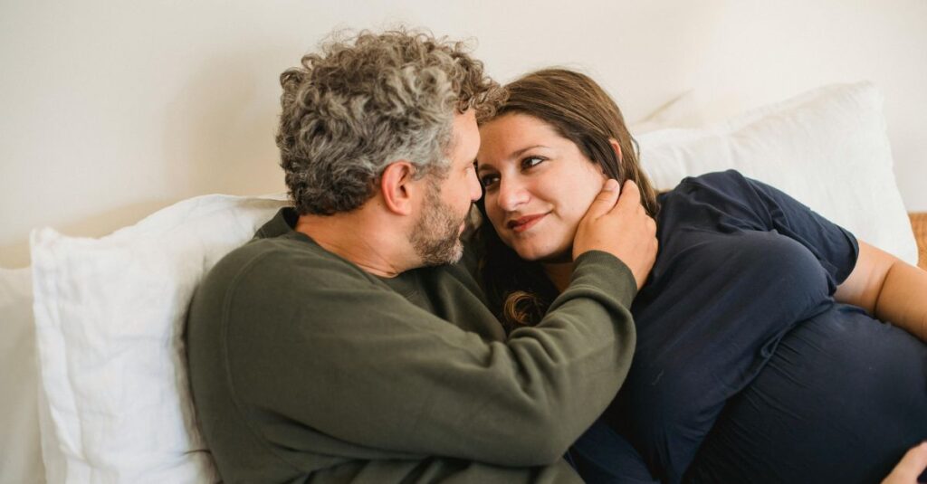 Expecting couple lays in bed with loving looks in their eyes.