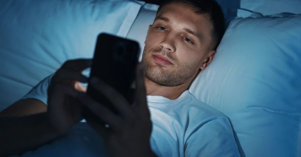 A man lying in bed at night, looking at his phone, illustrating how screen time can interfere with intimacy and connection.