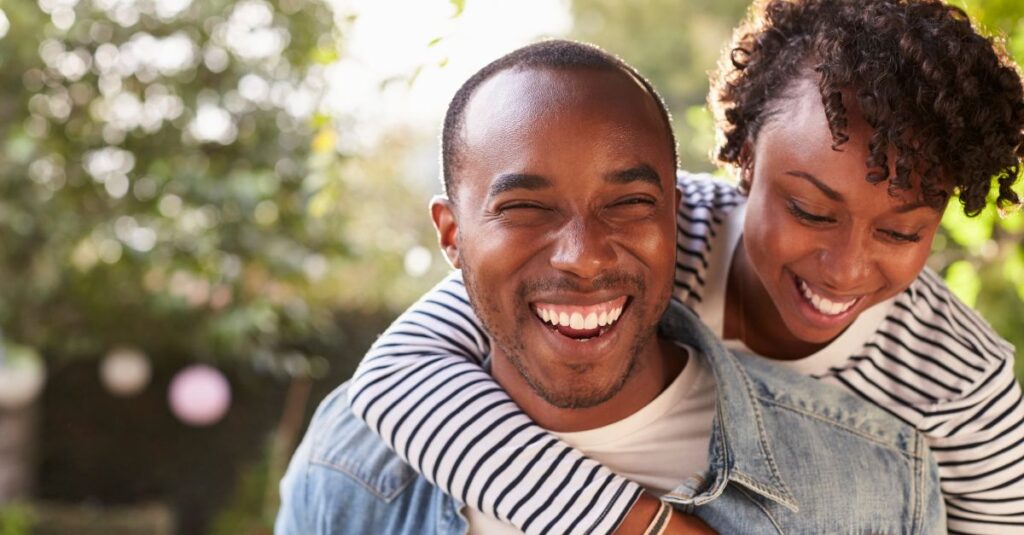 Happy couple outdoors, laughing and embracing, symbolizing trust and emotional closeness in a healthy relationship.