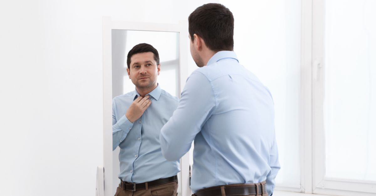 Professional man in the mirror looking reflective despite appearing confident, representing the contrast between outward success and inner insecurity.