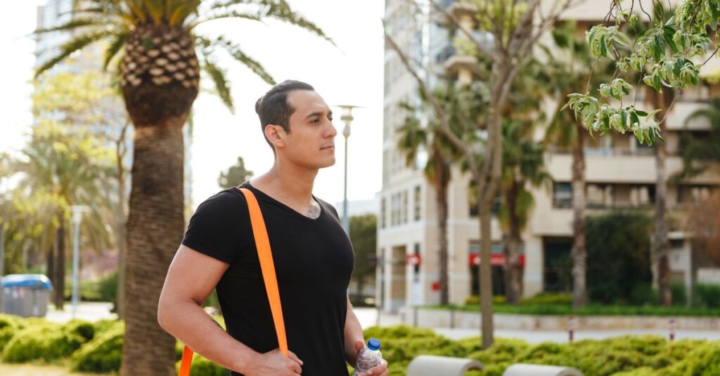 Confident man walking outdoors with a gym bag and water bottle, symbolizing strength, self-care, and positive mental health.