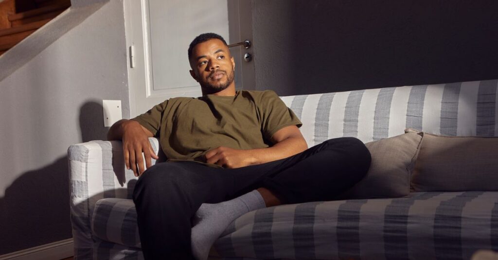 Man sitting alone on a couch in soft light, appearing deep in thought and emotionally distant, symbolizing the hidden exhaustion of high-functioning depression.