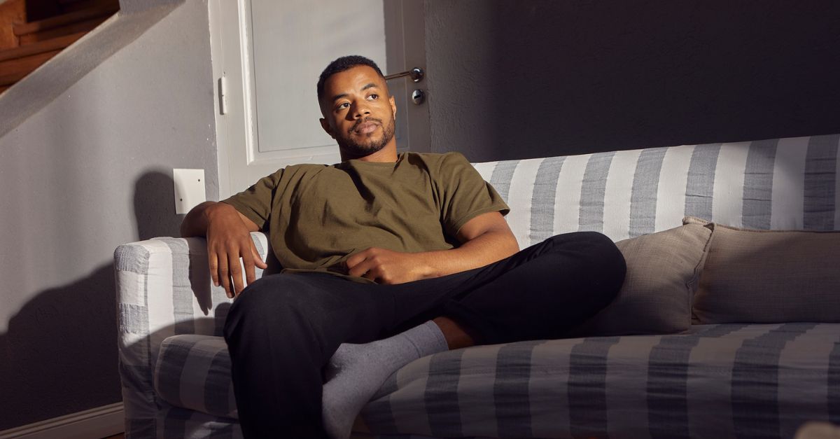 Man sitting alone on a couch in soft light, appearing deep in thought and emotionally distant, symbolizing the hidden exhaustion of high-functioning depression.