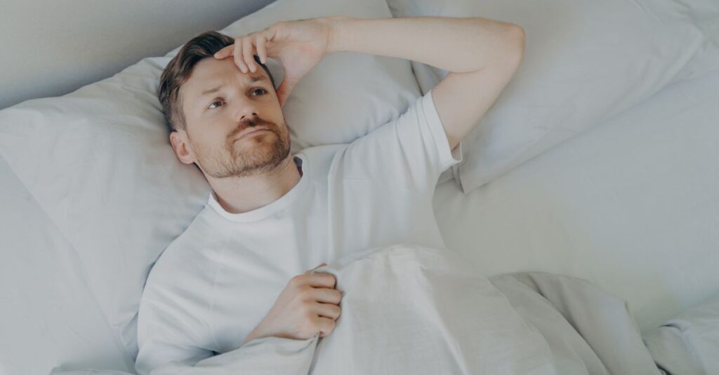 Man laying in bed at night, looking thoughtful and restless, representing anxiety and overthinking before sleep.