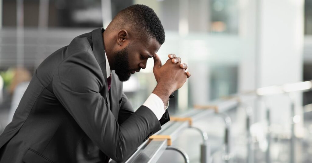 Man sitting with head bowed and hands clasped, reflecting stress and frustration — symbolizing anger management counseling for men in Massachusetts