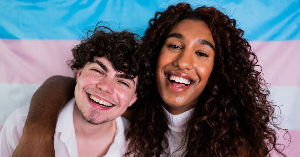 Transgender men smiling confidently in front of the transgender flag, representing empowerment and holistic sexual wellness.