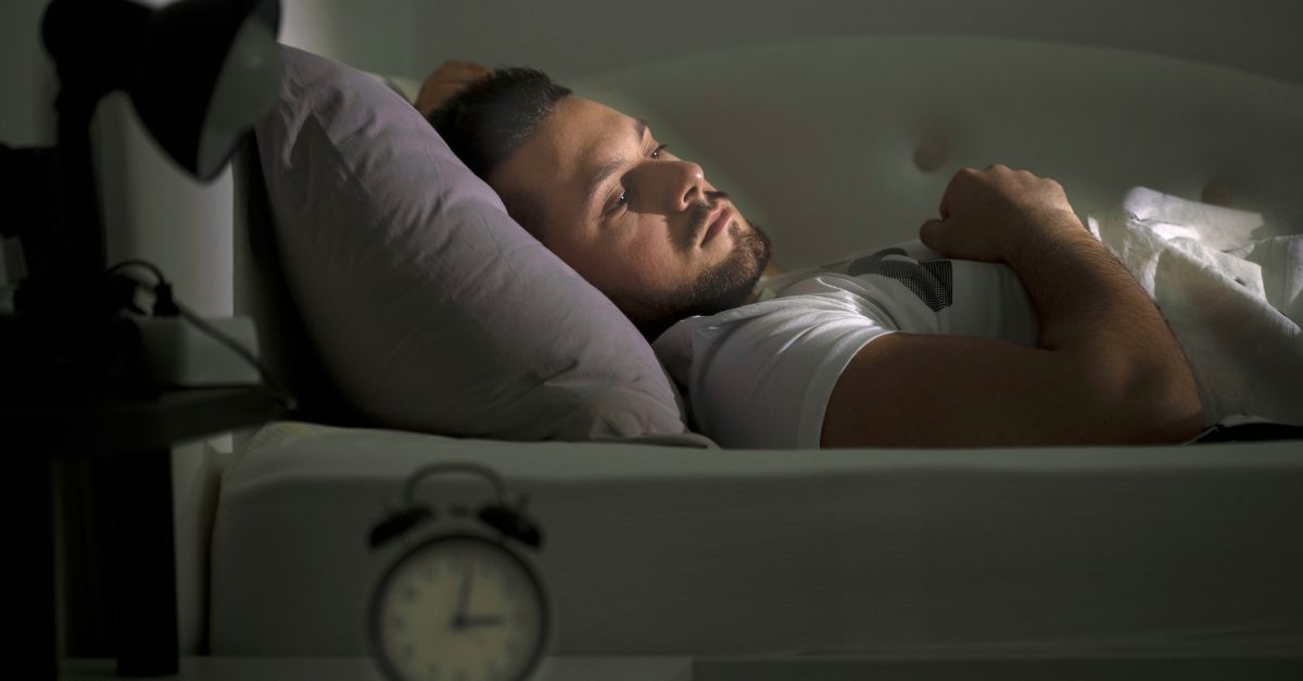 Man awake at 3 AM in bed with racing thoughts and anxiety unable to sleep.