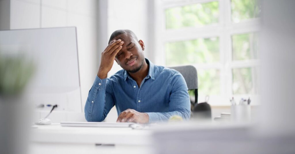Man sits at his desk with his hand on his forehead exhibiting signs of stress.