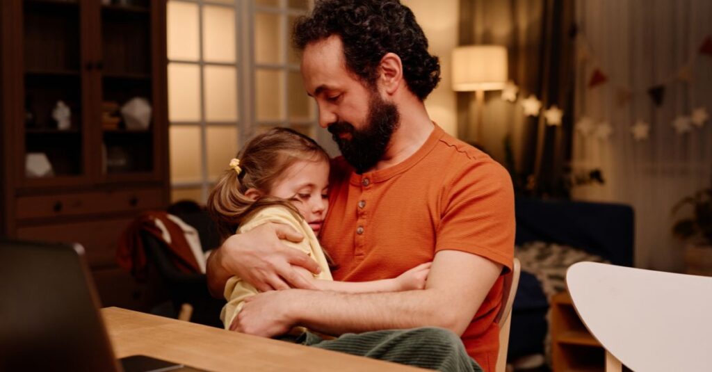 Father embraces his daughter, looking at her with endearment.