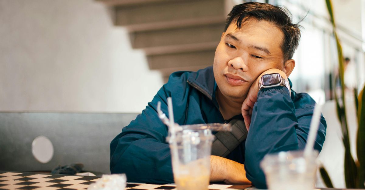 Man sitting alone at a table, leaning his face on his hand, with a thoughtful look on his face.