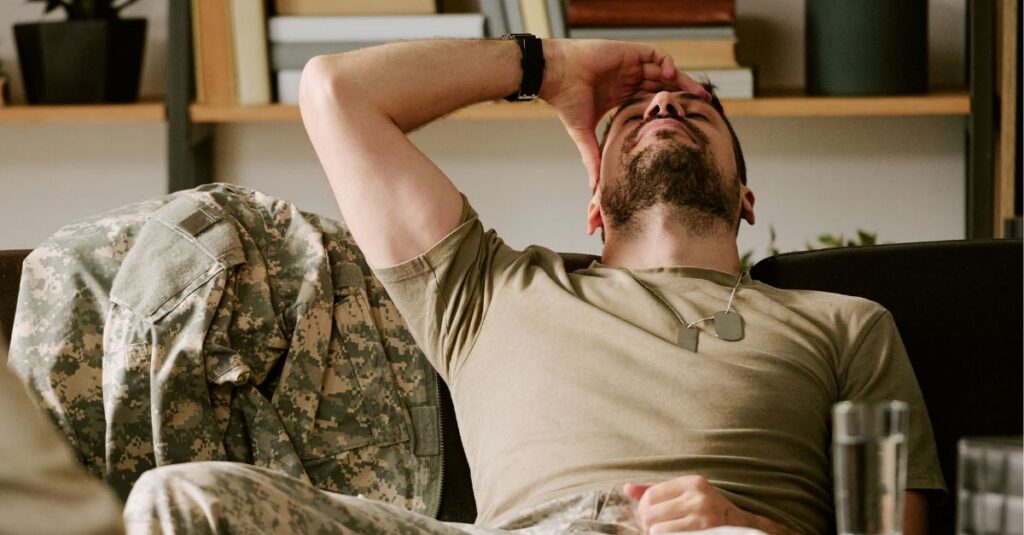 Veteran leans back on the couch as though exasperated or stressed with his hand on his head.