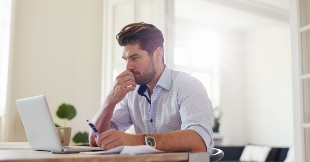Man sits at a desk looking at his laptop with an intense look of concentration on his face
